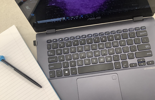 Overhead shot of a notebook, pen, and open laptop.